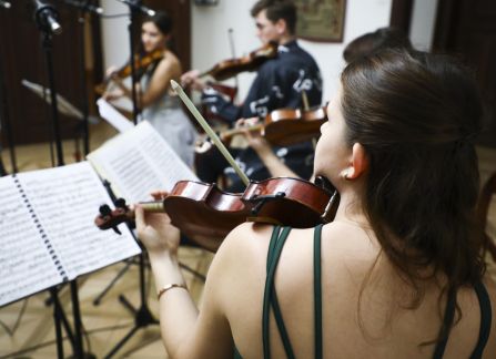 A photograph. A string concert in Villa Decius. The musicians play the violin and the cello in the Ball Room at Villa Decius.